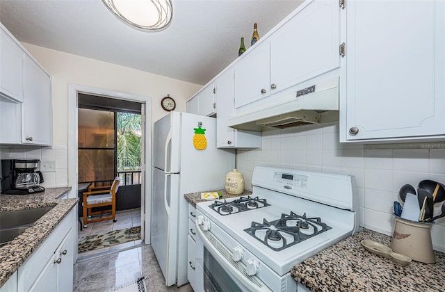 kitchen with white cabinets, white range, light tile flooring, backsplash, and dark stone countertops