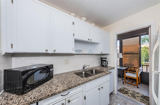 kitchen featuring light tile flooring, tasteful backsplash, white cabinetry, dark stone countertops, and sink