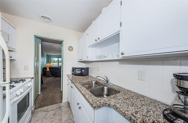 kitchen featuring backsplash, light tile flooring, white range with gas stovetop, white cabinets, and sink