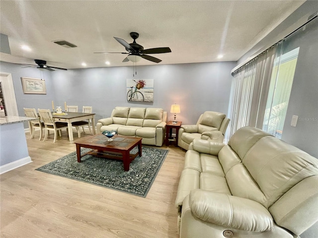 living room featuring a textured ceiling, light hardwood / wood-style flooring, and ceiling fan