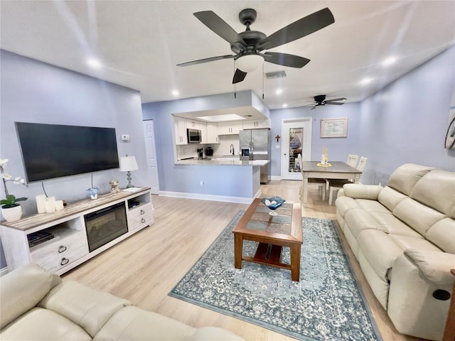 living room featuring ceiling fan, sink, and light hardwood / wood-style flooring