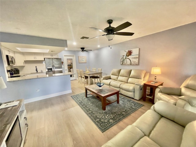 living room featuring a skylight, ceiling fan, and light hardwood / wood-style flooring