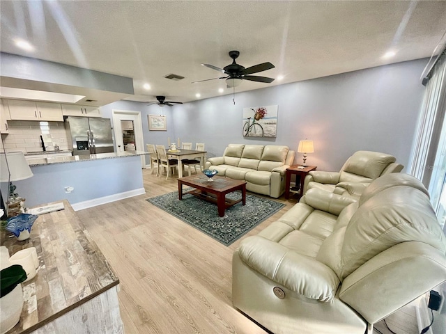 living room with a textured ceiling, ceiling fan, and light hardwood / wood-style floors