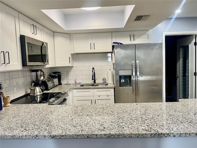 kitchen featuring appliances with stainless steel finishes, light stone counters, a raised ceiling, and white cabinetry