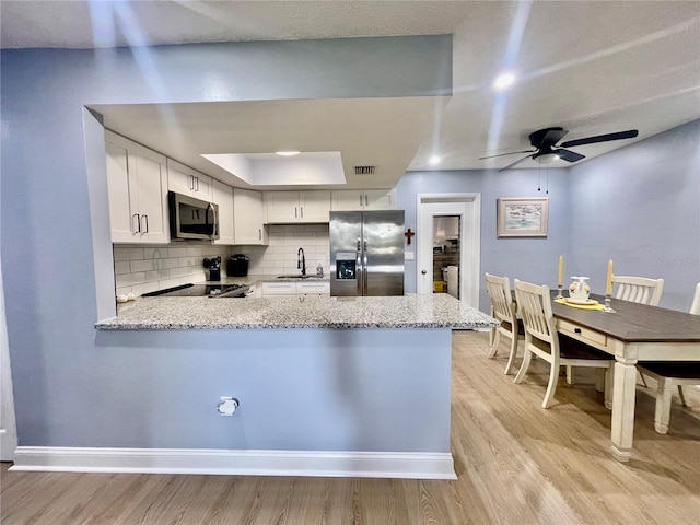 kitchen with appliances with stainless steel finishes, light stone counters, white cabinetry, and kitchen peninsula