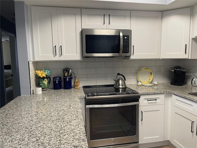 kitchen featuring light stone countertops, appliances with stainless steel finishes, white cabinetry, and decorative backsplash