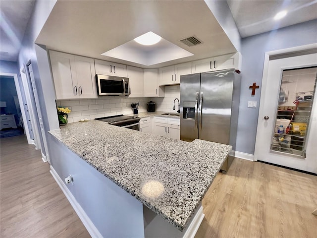 kitchen featuring light stone countertops, light hardwood / wood-style flooring, appliances with stainless steel finishes, kitchen peninsula, and white cabinetry