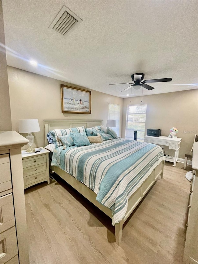 bedroom with a textured ceiling, light hardwood / wood-style flooring, and ceiling fan