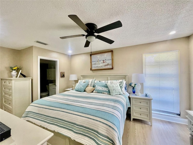 bedroom with light wood-type flooring, a textured ceiling, ensuite bathroom, and ceiling fan