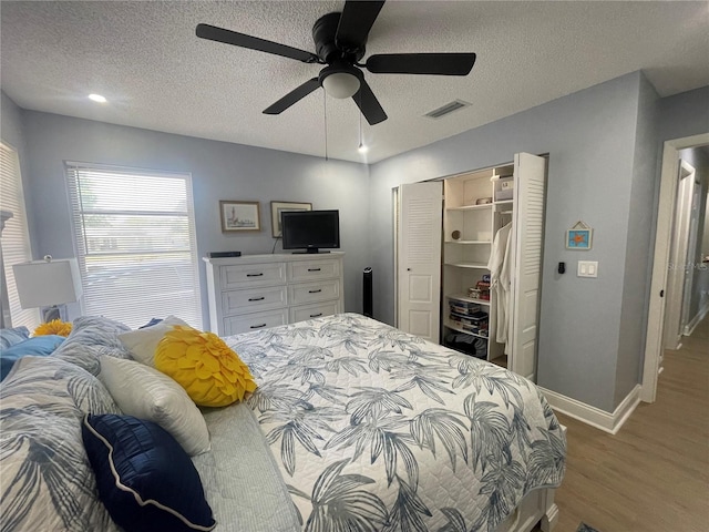 bedroom with a textured ceiling, ceiling fan, a closet, and hardwood / wood-style flooring