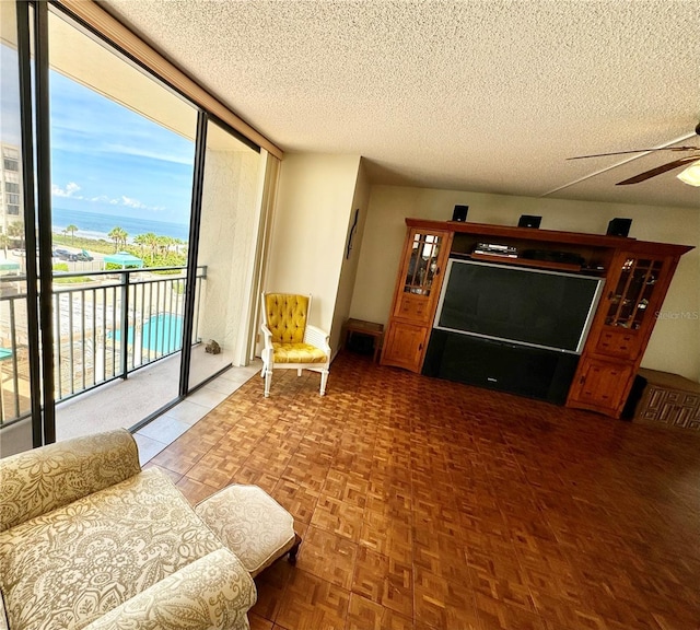 living room with a textured ceiling, baseboards, a wall of windows, and a ceiling fan