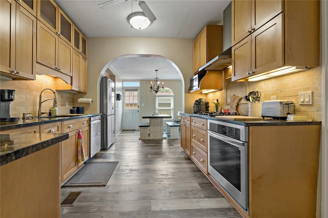 kitchen with decorative light fixtures, appliances with stainless steel finishes, ceiling fan with notable chandelier, tasteful backsplash, and hardwood / wood-style flooring