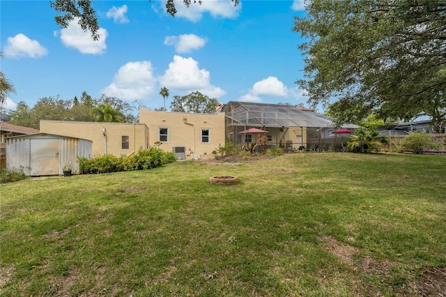 view of yard featuring a fire pit, glass enclosure, and a storage unit