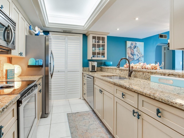 kitchen featuring stainless steel appliances, sink, light stone countertops, and a raised ceiling