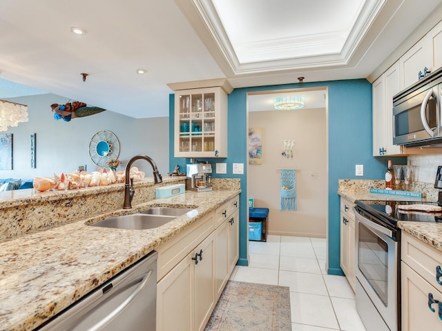 kitchen with appliances with stainless steel finishes, a tray ceiling, light stone counters, sink, and light tile flooring