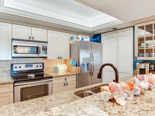 kitchen with stainless steel appliances, tasteful backsplash, a raised ceiling, crown molding, and light stone countertops