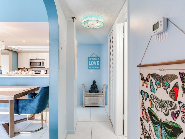 hall with a tray ceiling, a textured ceiling, and light tile floors