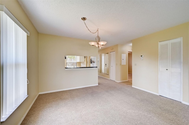 spare room with a textured ceiling, carpet floors, and a chandelier