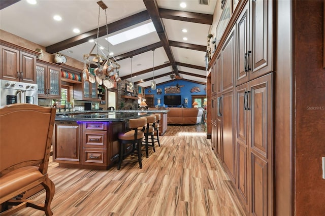 kitchen with a breakfast bar, decorative light fixtures, glass insert cabinets, open floor plan, and dark stone counters