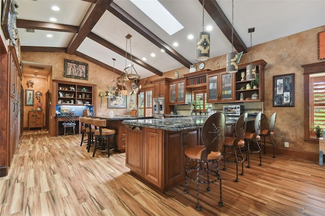 bar with hanging light fixtures, a skylight, light wood finished floors, and beamed ceiling