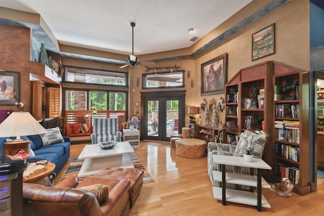 living room with a ceiling fan, a towering ceiling, light wood-style flooring, a textured ceiling, and french doors