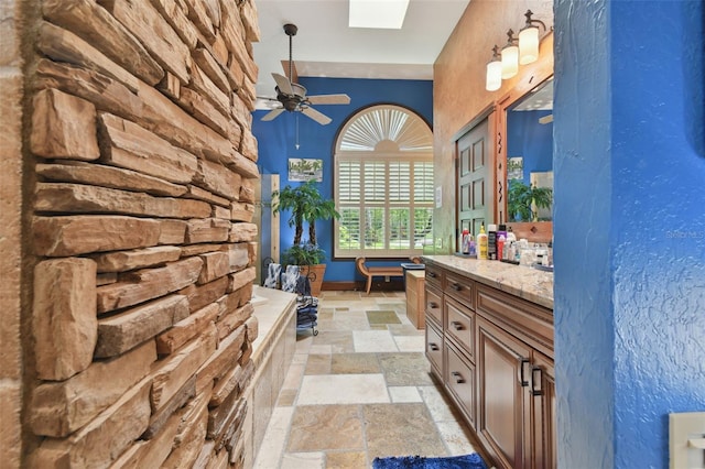 bathroom featuring ceiling fan, a skylight, vanity, and stone tile flooring