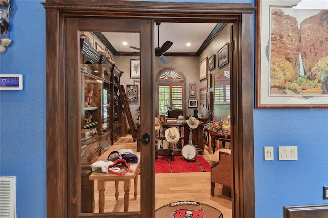 interior space featuring visible vents, a ceiling fan, a textured wall, wood finished floors, and crown molding