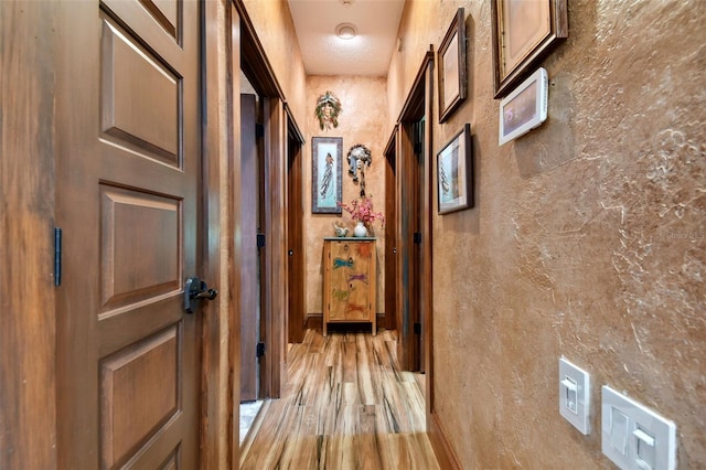 hallway featuring light wood-type flooring and a textured wall