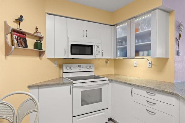 kitchen featuring white cabinets, light stone counters, and white appliances