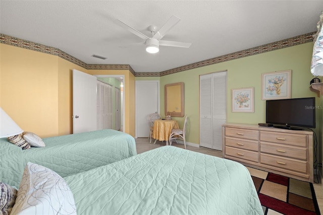 bedroom featuring ceiling fan, light tile floors, and two closets