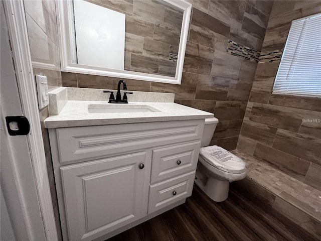 bathroom with tile walls, walk in shower, large vanity, toilet, and wood-type flooring