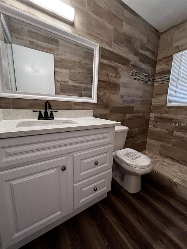 bathroom with wood-type flooring, tile walls, toilet, and vanity with extensive cabinet space