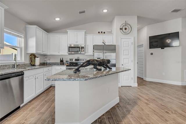 kitchen with light hardwood / wood-style flooring, white cabinetry, appliances with stainless steel finishes, a kitchen island, and lofted ceiling