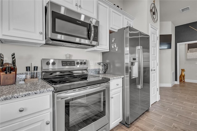 kitchen with appliances with stainless steel finishes, light hardwood / wood-style flooring, light stone countertops, and white cabinets