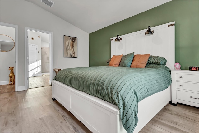 bedroom with light hardwood / wood-style flooring, vaulted ceiling, and ensuite bathroom