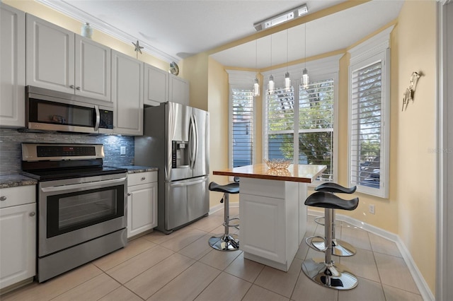 kitchen with appliances with stainless steel finishes, a breakfast bar area, tasteful backsplash, and white cabinets