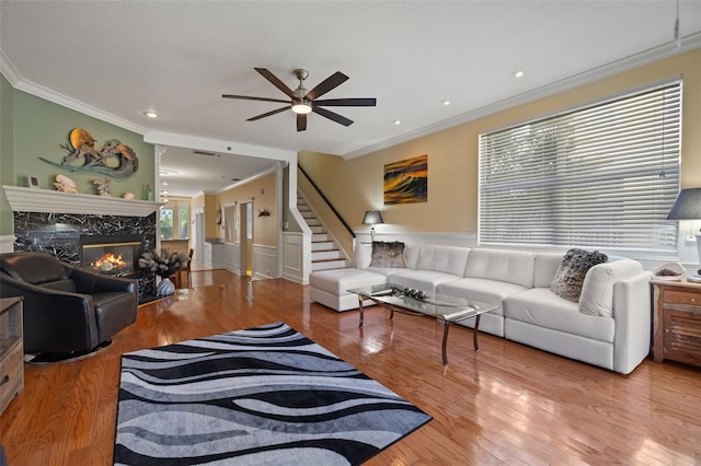 living room featuring ornamental molding, a premium fireplace, wood-type flooring, and ceiling fan