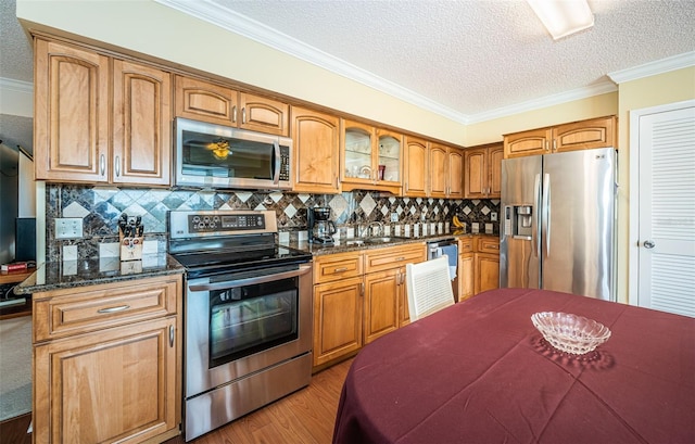 kitchen featuring crown molding, dark stone countertops, stainless steel appliances, tasteful backsplash, and a textured ceiling