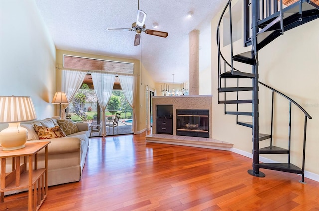 living room featuring a textured ceiling, hardwood / wood-style floors, ceiling fan, a tiled fireplace, and high vaulted ceiling