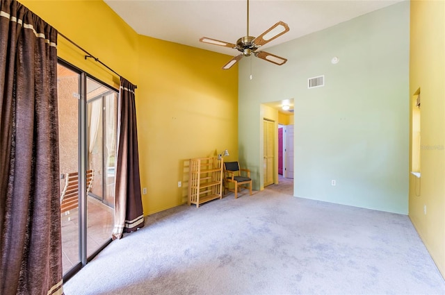 carpeted empty room with a towering ceiling and ceiling fan