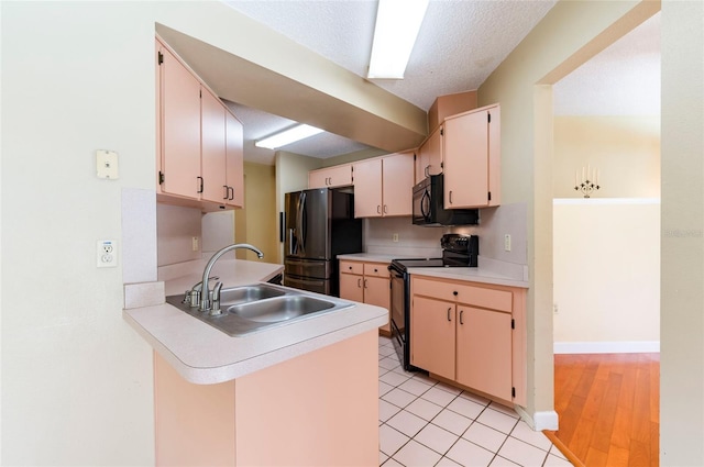 kitchen with kitchen peninsula, light wood-type flooring, black appliances, cream cabinetry, and sink