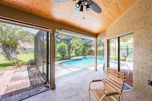 view of swimming pool with a patio area, glass enclosure, and ceiling fan