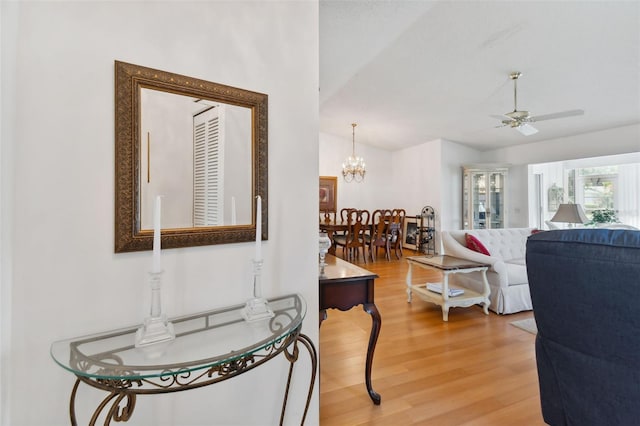 living room with vaulted ceiling, ceiling fan with notable chandelier, and wood-type flooring