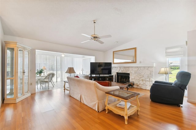 living room with ceiling fan, vaulted ceiling, a stone fireplace, and light hardwood / wood-style floors