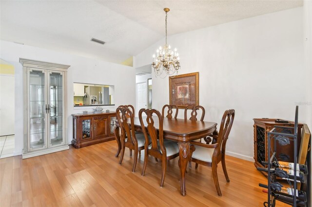 dining space featuring vaulted ceiling, a chandelier, and light hardwood / wood-style flooring