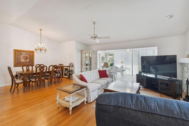 living room with ceiling fan with notable chandelier, lofted ceiling, and light hardwood / wood-style floors