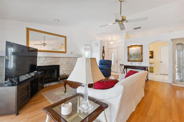 living room with ceiling fan, vaulted ceiling, a stone fireplace, and light hardwood / wood-style flooring