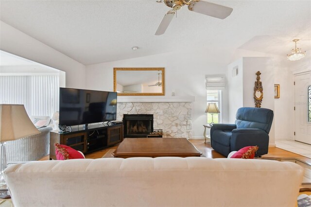 living room featuring ceiling fan, vaulted ceiling, a stone fireplace, and light hardwood / wood-style flooring