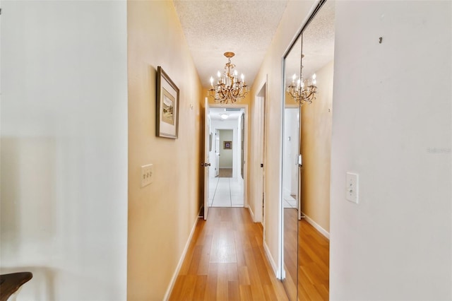 hall with a textured ceiling, hardwood / wood-style flooring, and a notable chandelier