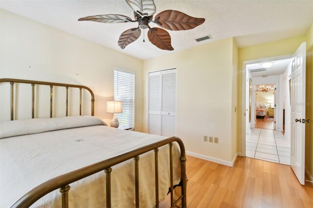 bedroom featuring ceiling fan with notable chandelier, light hardwood / wood-style floors, a textured ceiling, and a closet